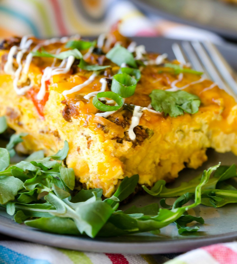 A square of yellow colored Overnight_Mexican_Breakfast_Casserole atop a bed of greens on a plate
