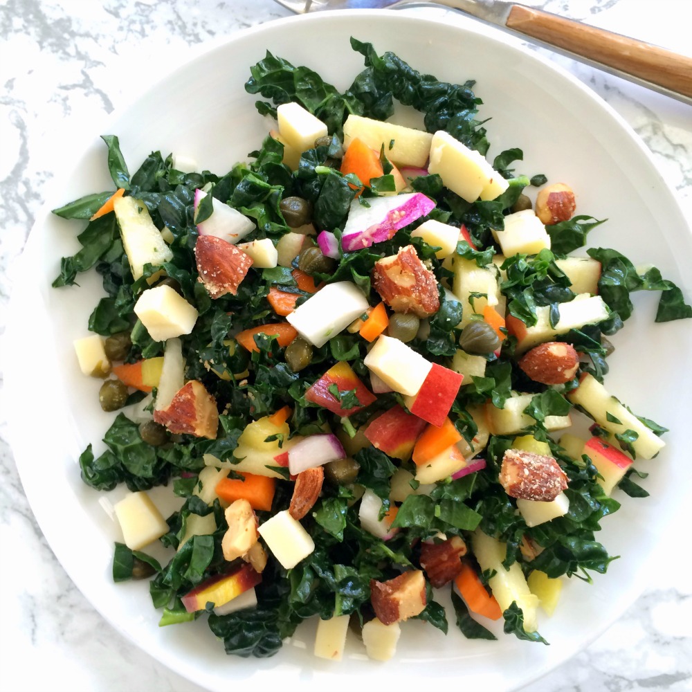 Kale Salad with diced vegetables and fruits on a white plate