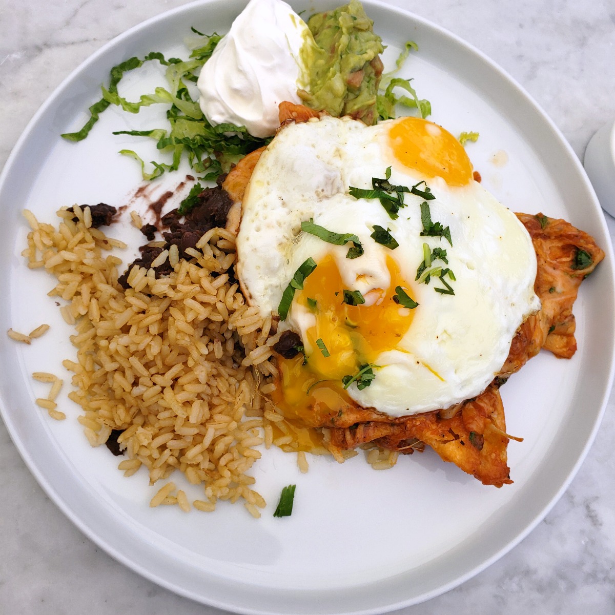 Chilaquiles with fried eggs on top, rice and guacamole alongside on a white plate at The Sparrow Cafe in Malibu