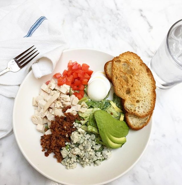 Piles of chicken, bacon, blue cheese, avocado, tomato and sliced egg on a white plate with 2 pieces of toast alongside at The Sparrow Cafe in Malibu