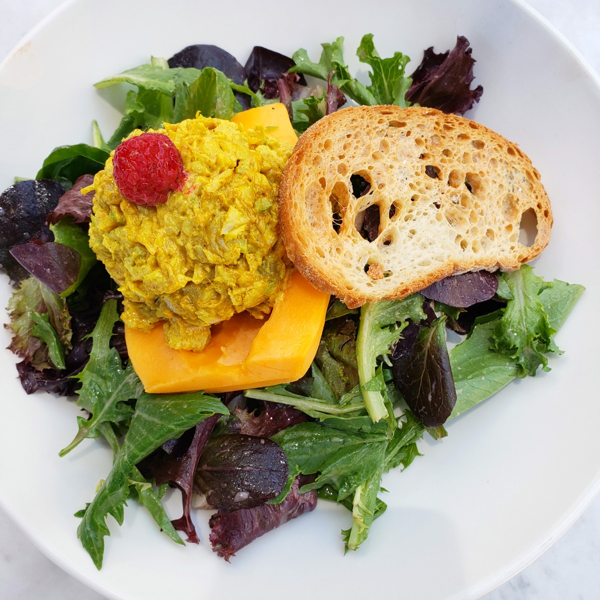 Papaya Curried Chicken Salad atop mixed greens in a white bowl at The Sparrow Cafe in Malibu