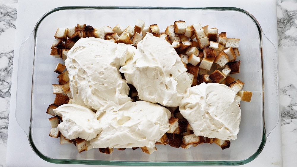 Dollops of cream cheese layer on top of diced cake cubes in a glass dish