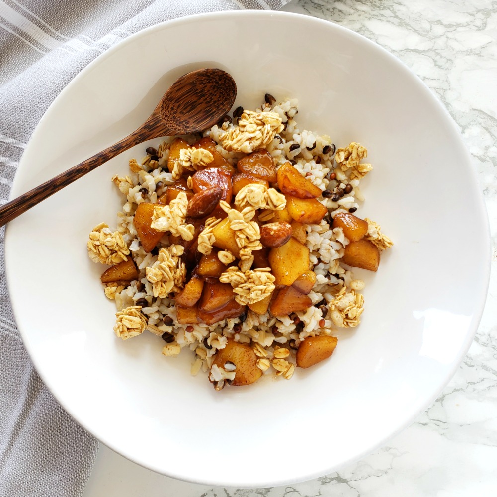 Apple Crisp Breakfast Bowl in a white bowl on a marble counter with a brown wooden spoon resting in the bowlm