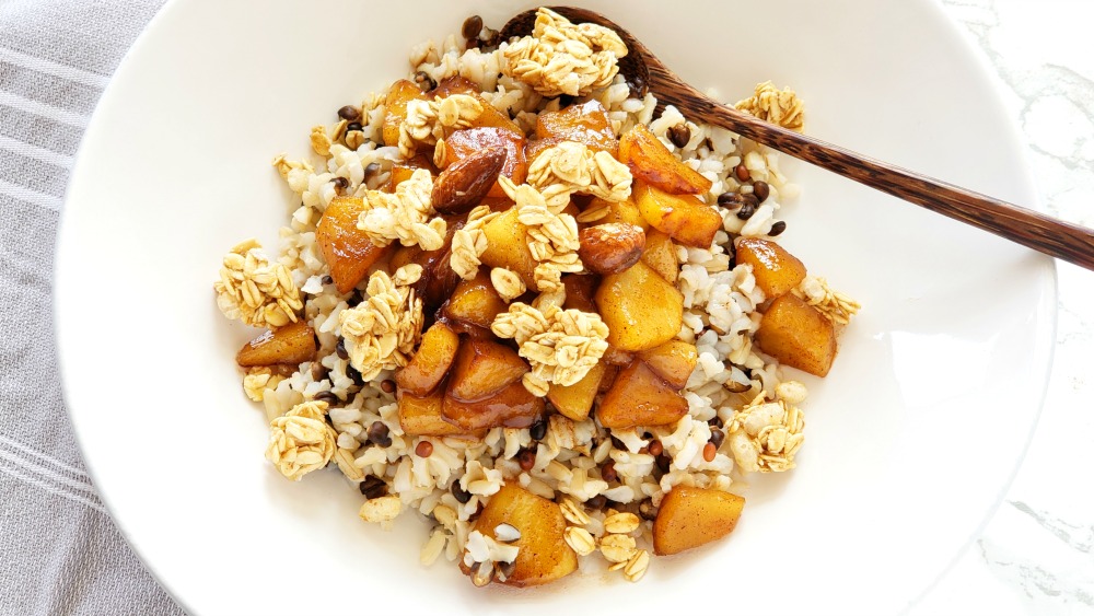 Apple Crisp Breakfast Bowl in a white bowl with wooden spoon, on a white marble counter and grey towel underneath