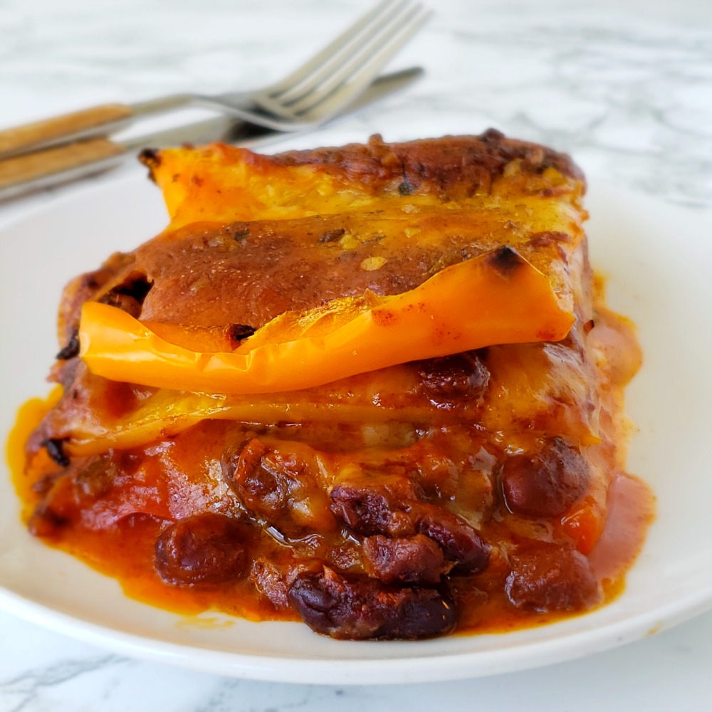 Layered 3-Ingredient Chili Cheese Peppers Casserole on a white plate with a fork and knife in background on a white marble counter
