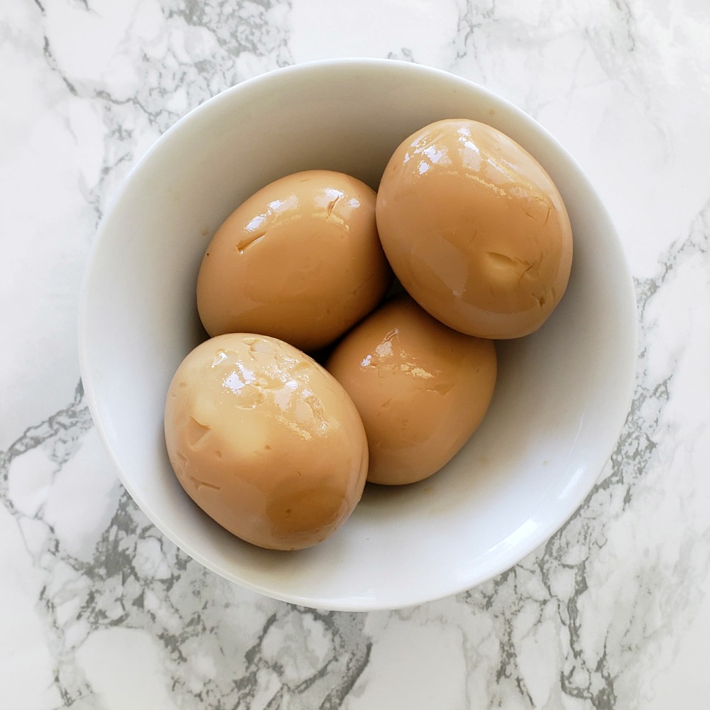 4 brown-colored hard-boiled eggs in a white bowl sitting on a white marble countertop