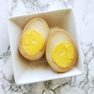Brown-tinged cut-open Soy-Brined Hard-Boiled Egg on a square white plate sitting on a white marble counter