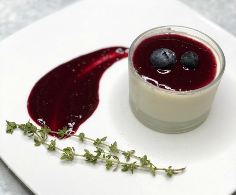 Berry Panna Cotta in a glass ramekin with a smear of berry puree beside it on a white plate, from The Black Trumpet restaurant on ShockinglyDelicious.com