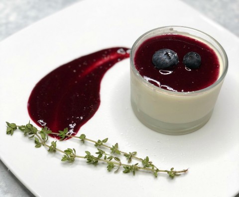 Panna Cotta de bayas en un recipiente de cristal con una capa de puré de bayas al lado en un plato blanco, del restaurante The Black Trumpet en ShockinglyDelicious.com