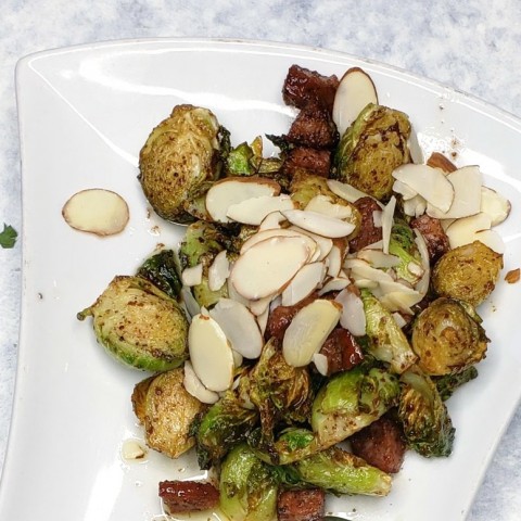 Brussels sprouts with chorizo and sumac vinaigrette with sliced almonds on top on a white plate on ShockinglyDelicious.com