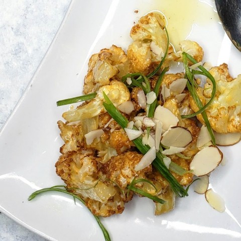 Coliflor con sriracha y alioli de harissa en un plato blanco con cebolletas encima en ShockinglyDelicious.com