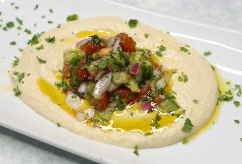 Dip de garbanzo humus en un plato blanco con perejil encima en ShockinglyDelicious.com
