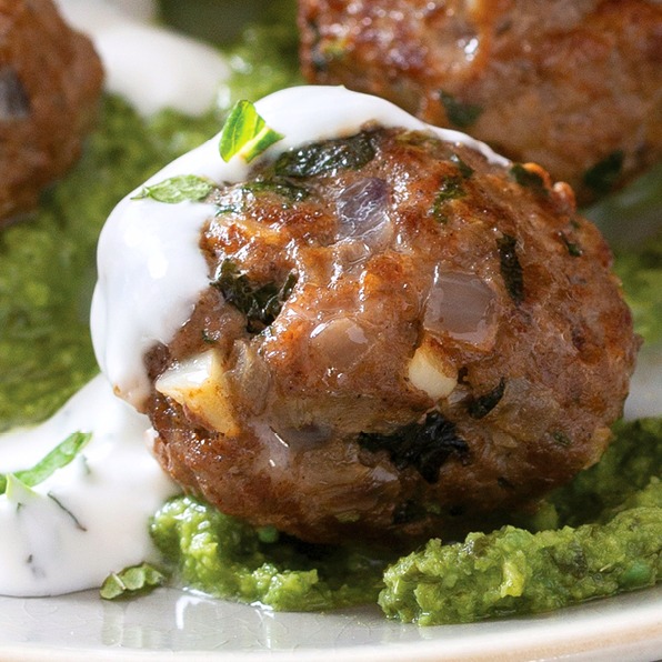 Lamb meatball with white sauce on top sitting on a white plate