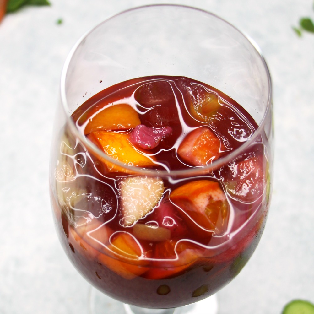 Merlot Sangria in a glass with fruit floating on top against a white background