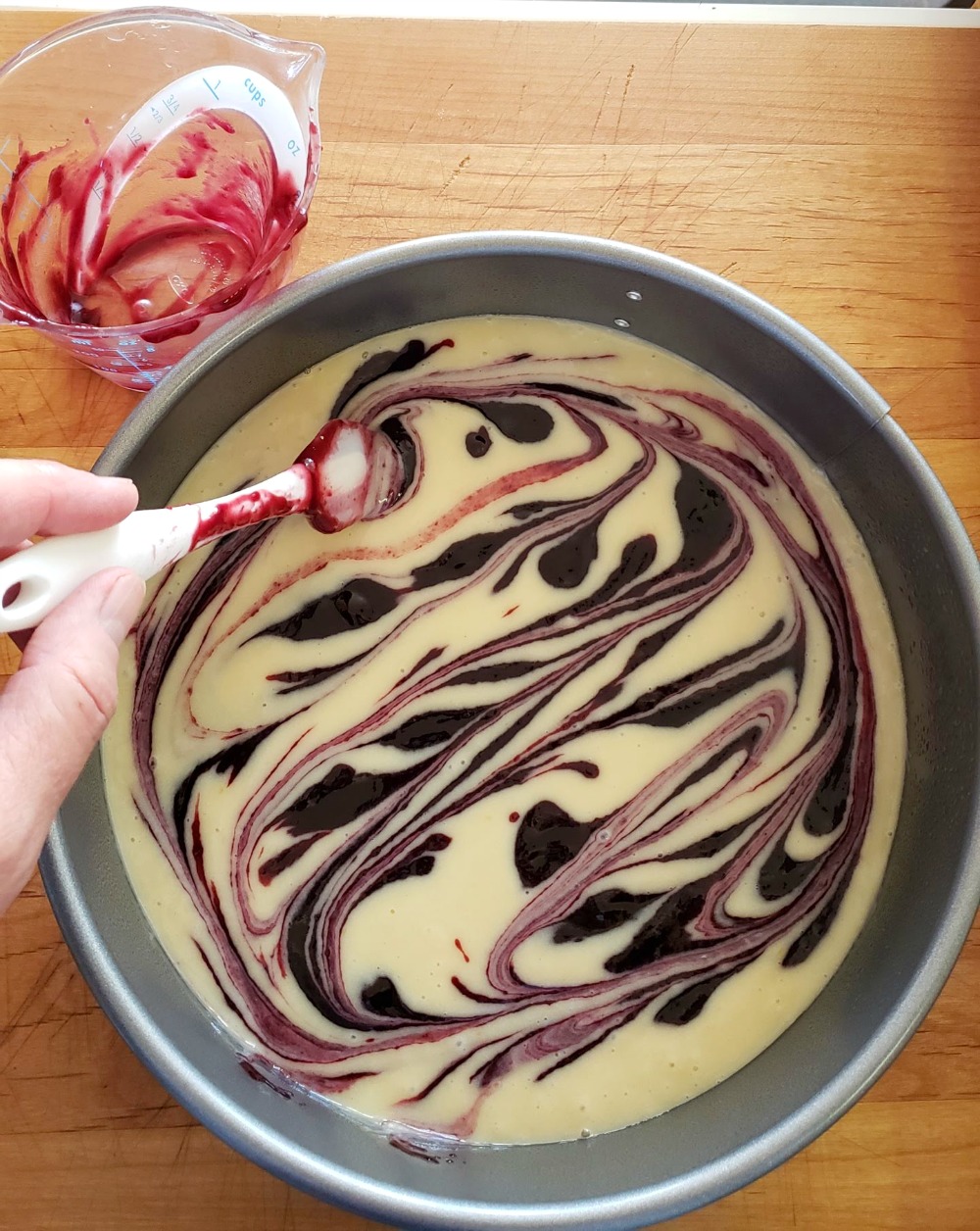 Hand holding small white spatula swirls jam into cake batter on Jam Breakfast Cake with Streusel on ShockinglyDelicious.com