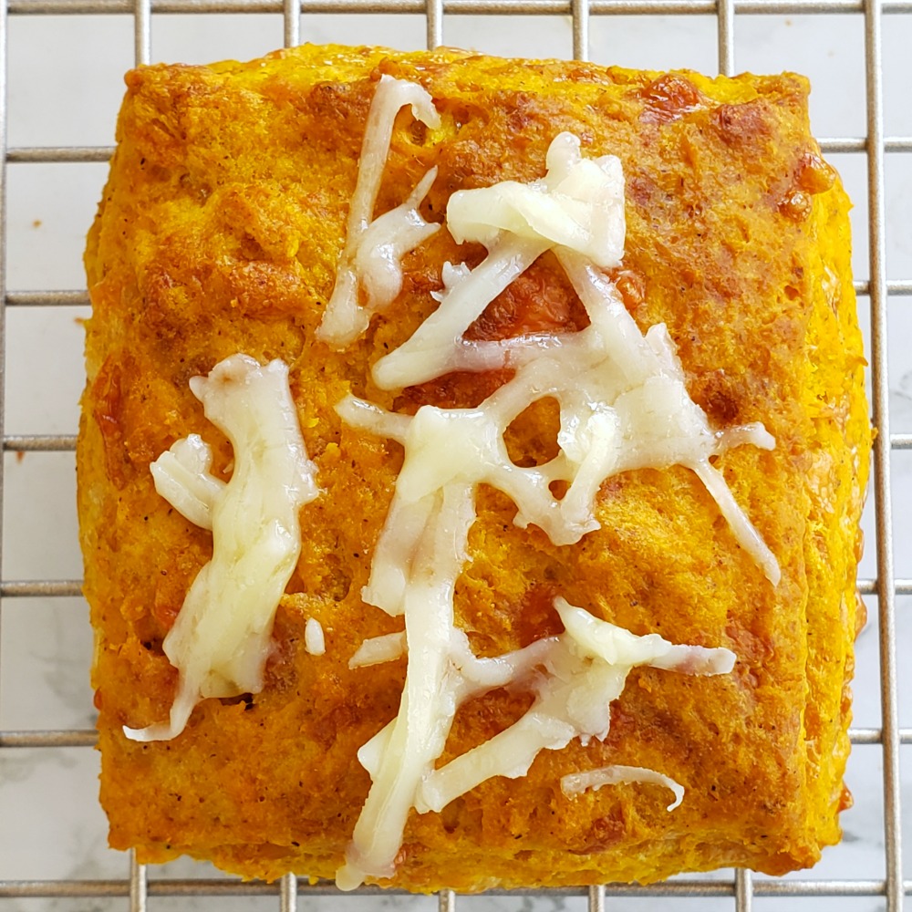Square orange Pumpkin Cheddar Biscuit with cheese on top on a gold wire cooling rack on ShockinglyDelicious.com