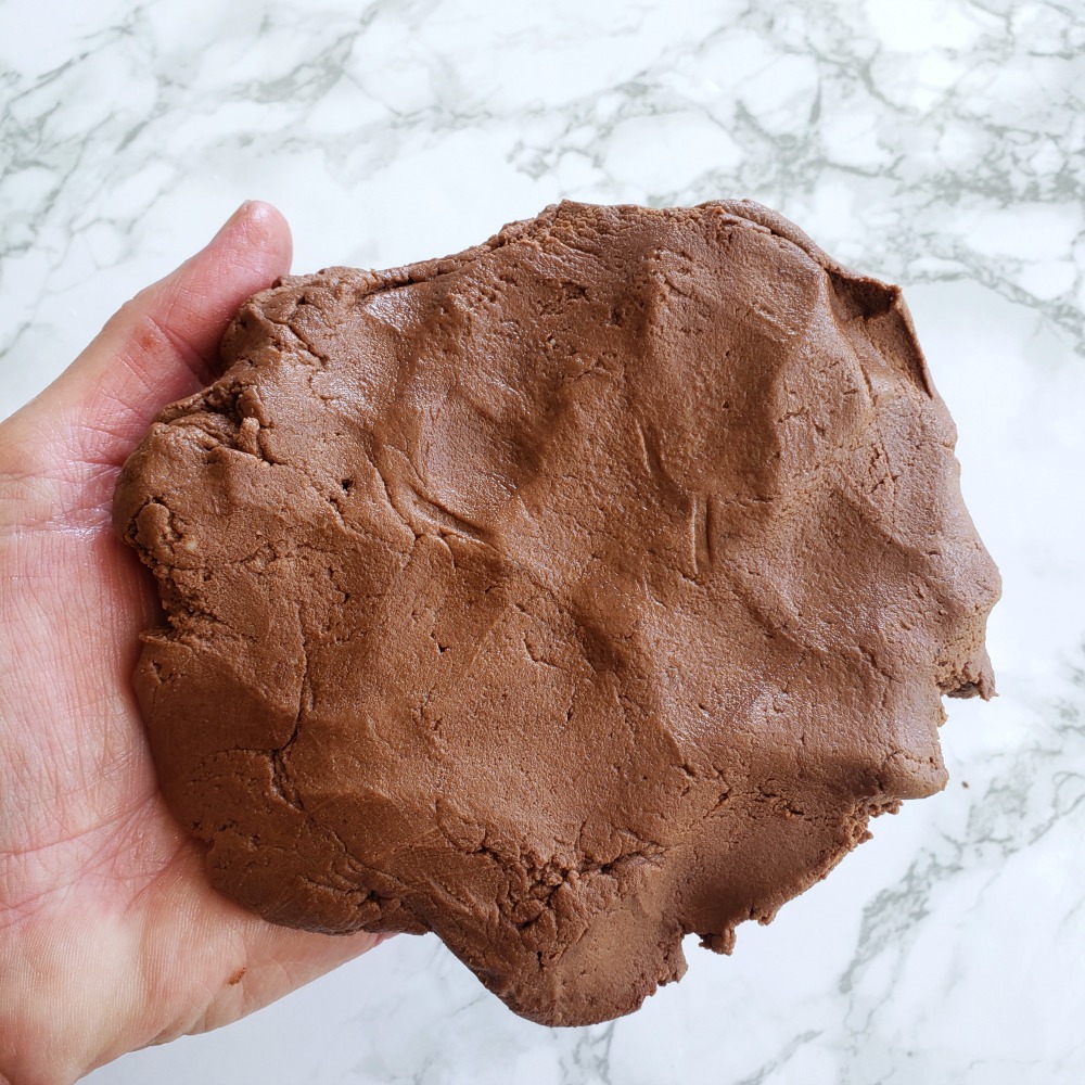 Rich Chocolate Shortbread Cookie dough held by a hand above a white marble counter top on ShockinglyDelicious.com