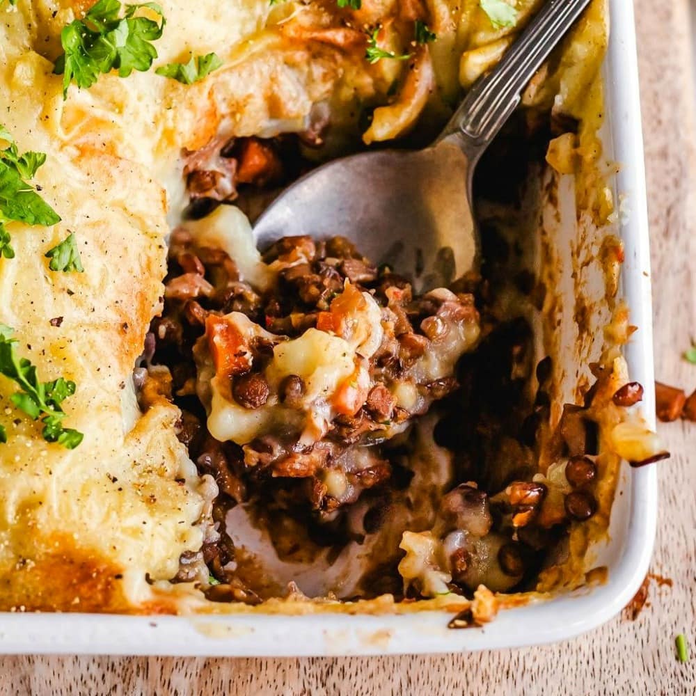 Large stainless steel serving spoon scoops out a portion of Lentil Mushroom Shepherd's Pie from a rectangular white baking dish