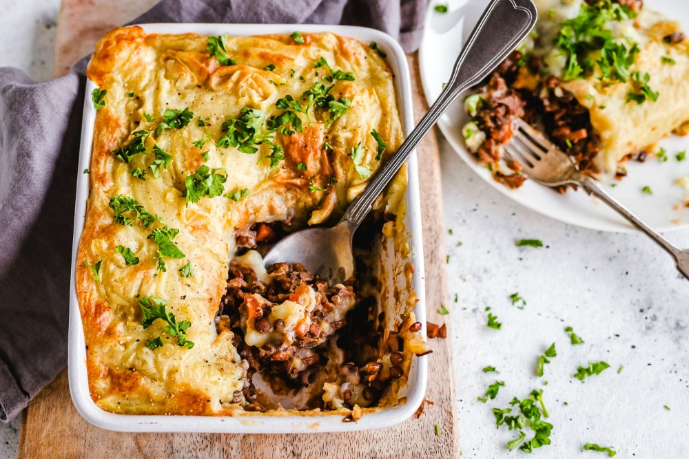 Lentil Mushroom Shepherd's Pie in a white rectangular baking dish with a spoon inside and a plate of the same food in the top right corner