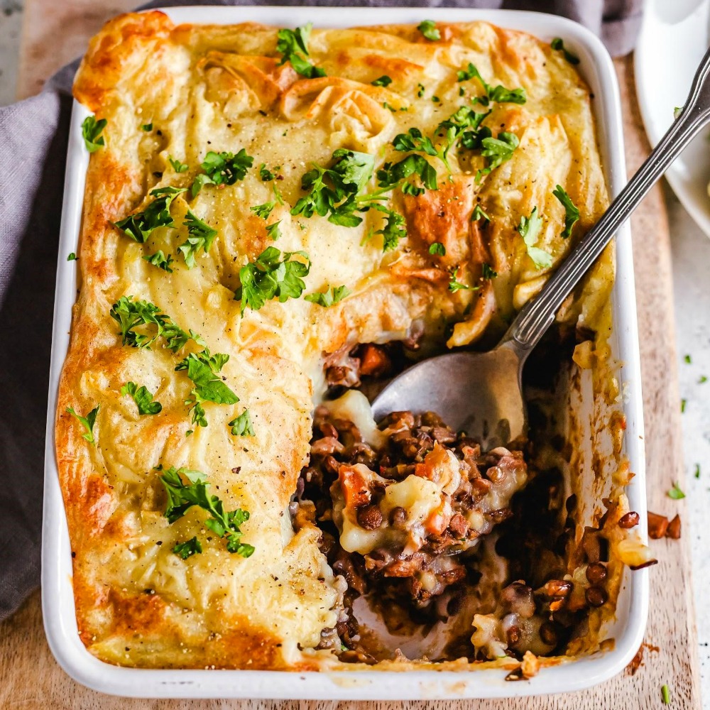 Vegan Lentil Mushroom Shepherd's Pie in a white casserole dish with a silver serving spoon