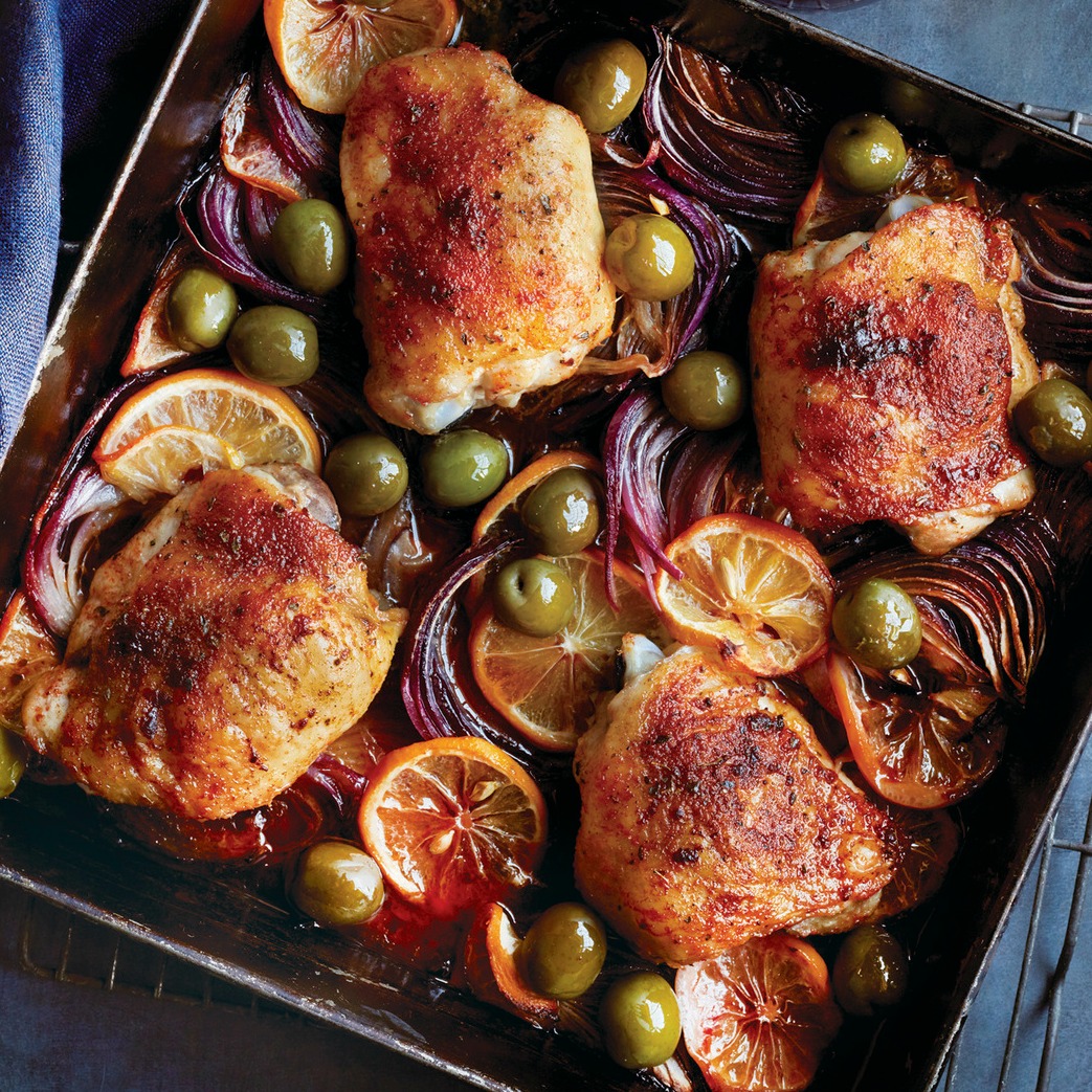 4 Roast Chicken thighs in a dark baking pan with lemon and onion slices