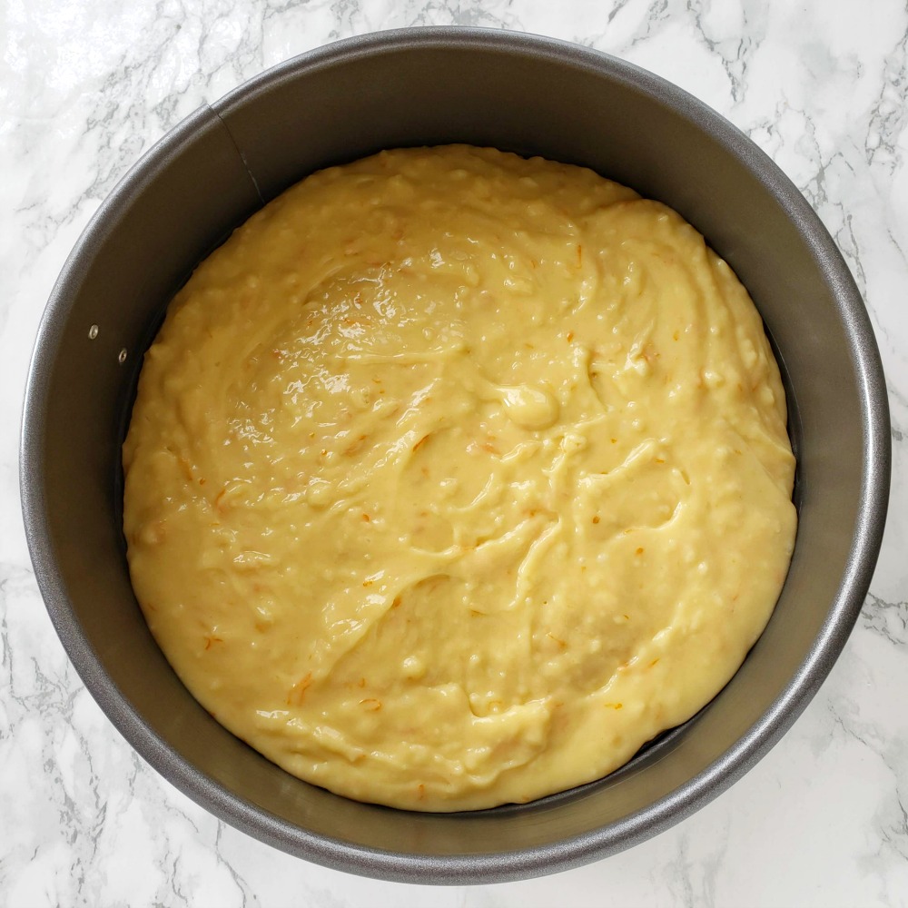 Grey springform pan with cake batter in it on a white marble counter