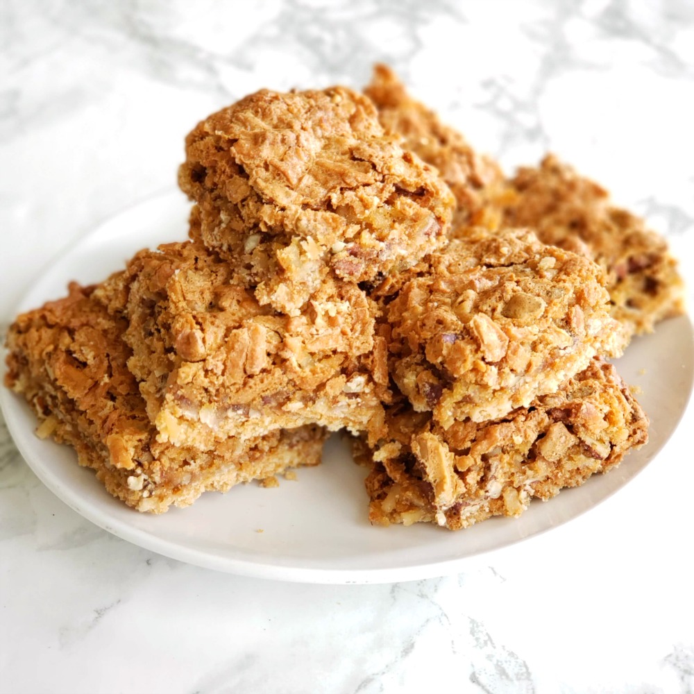 A stack of brown coconut pecan dream bars on a white plate on a white marble counter