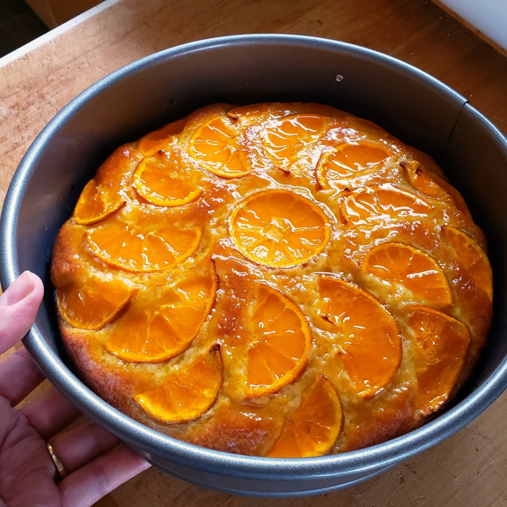 Glazed tangerine cake in a pan held by a hand