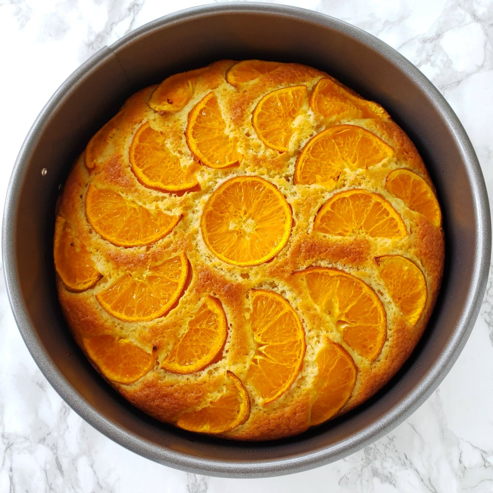 Baked cake in a gray pan is out of the oven and on a white marble counter