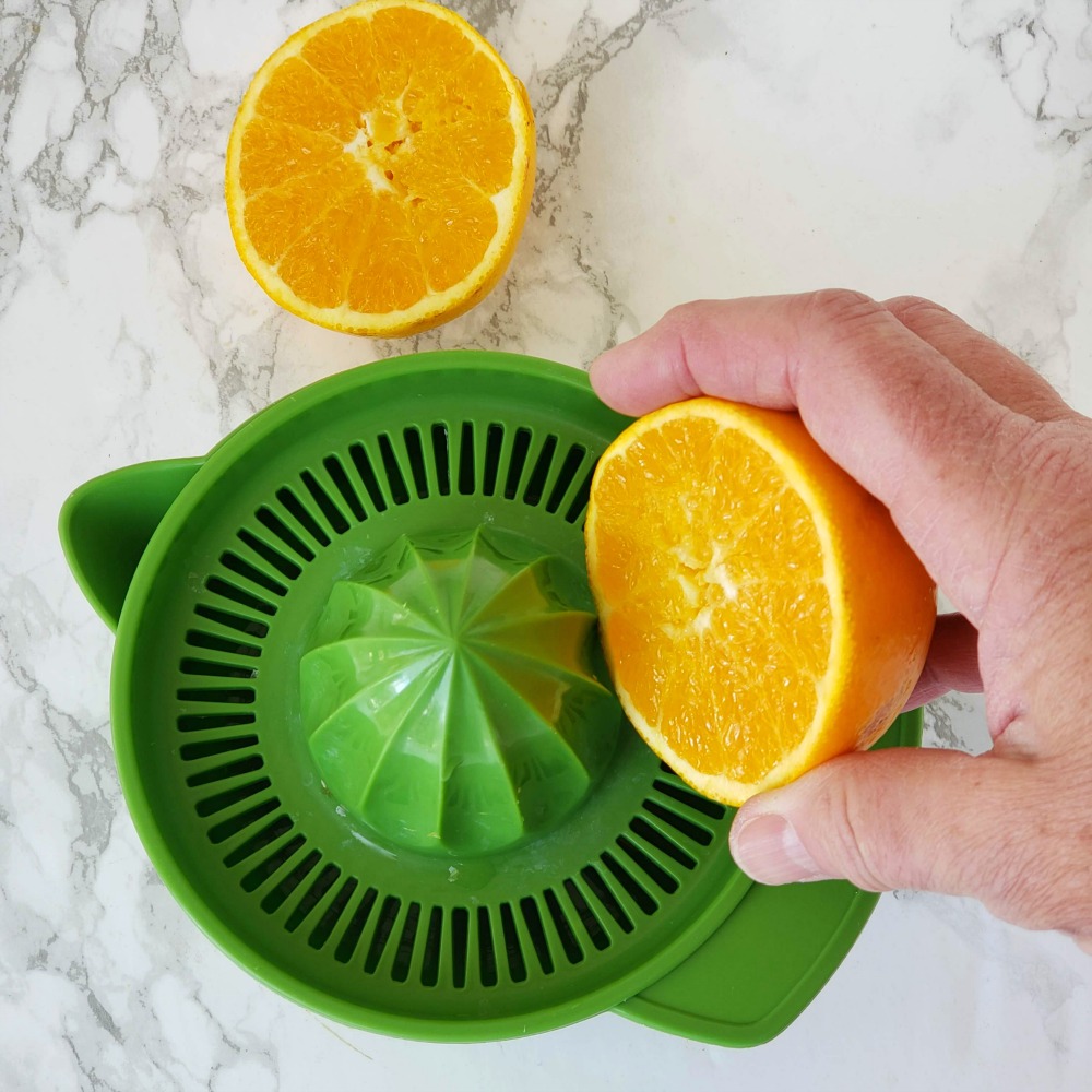 Juicing an orange in a green juicer on a white marble counter