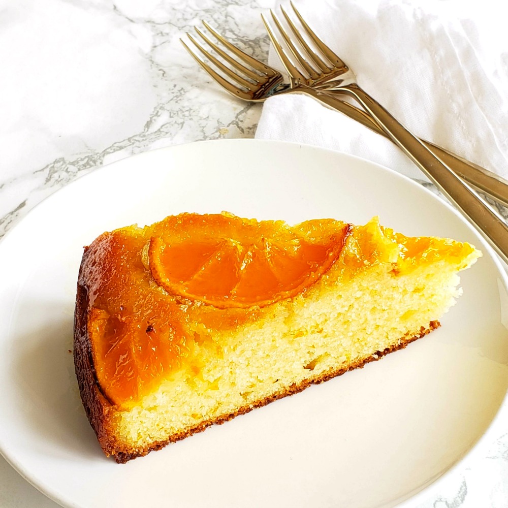Wedge of Greek Yogurt Tangerine Cake on a white plate with 2 forks to the right