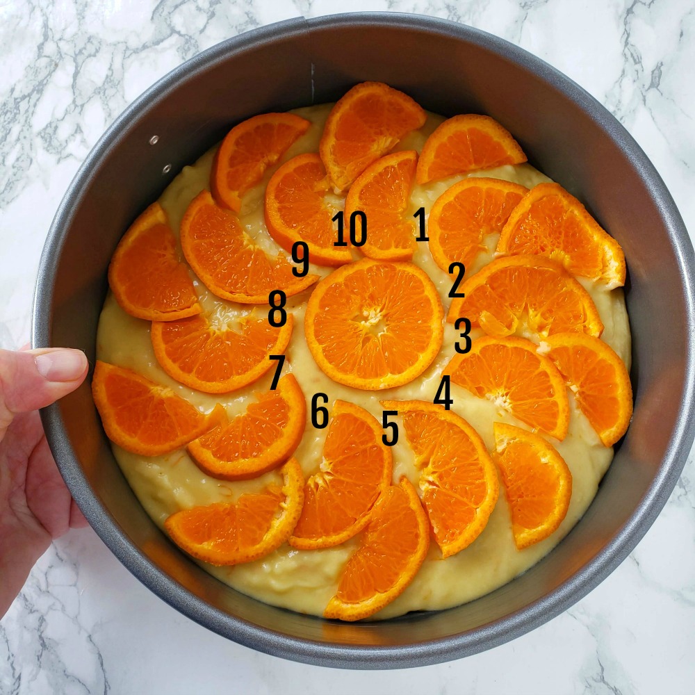Tangerine half moon slices on top of cake batter, with numbers indicating where cake will be cut. 