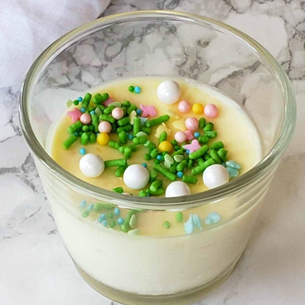 Orange Posset with sprinkles on top in glass cup on white marble counter