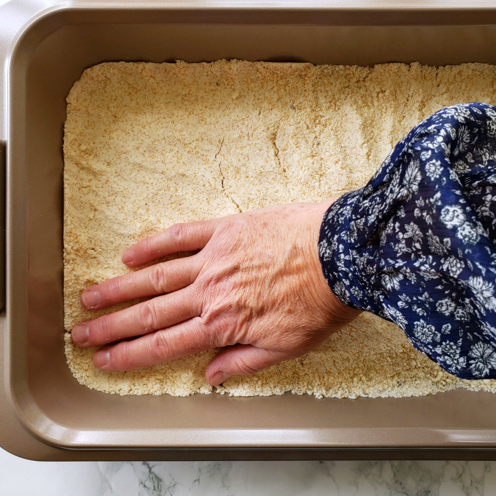 A hand pats crust into a baking pan