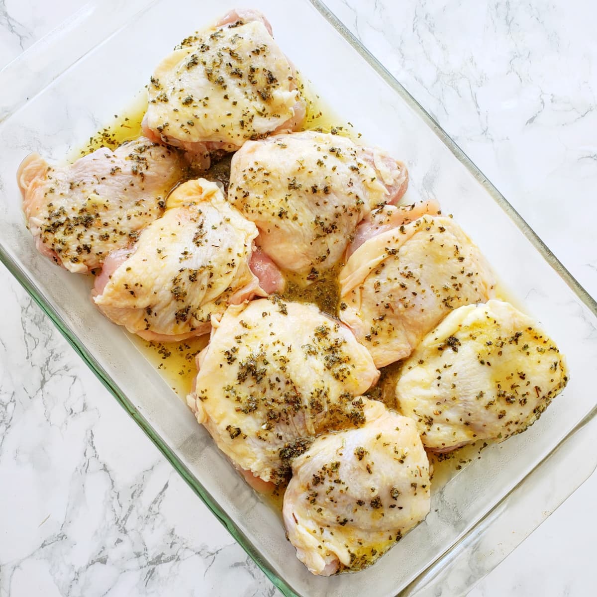 8 chicken thighs in a glass baking dish set on a white marble counter