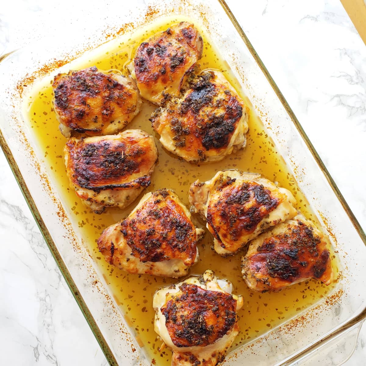 8 chicken thighs deeply brown from roasting, in a yellow sauce, with the pan set on a white marble counter