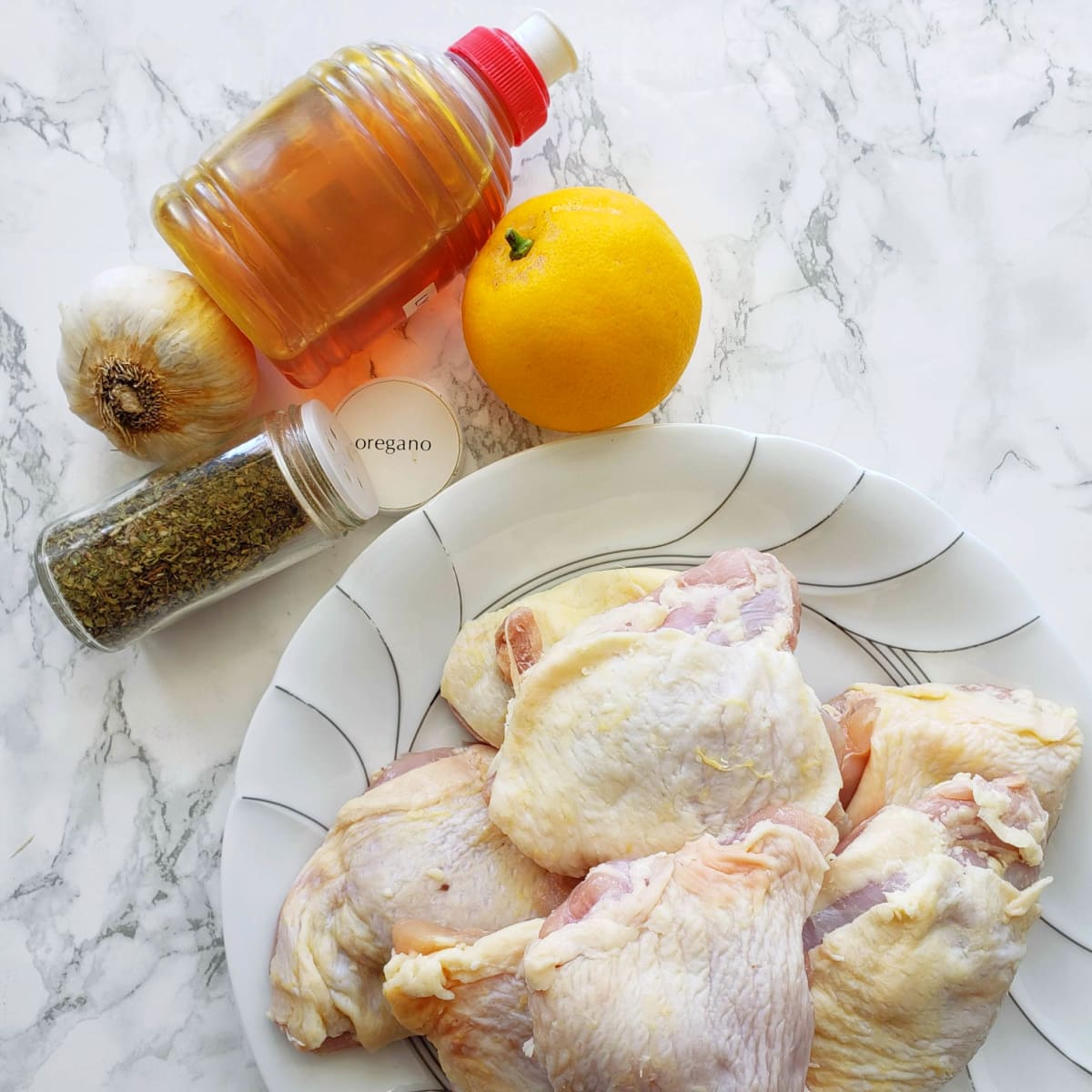 Ingredients for Sticky Lemon Oregano Chicken on a white plate on a white marble counter