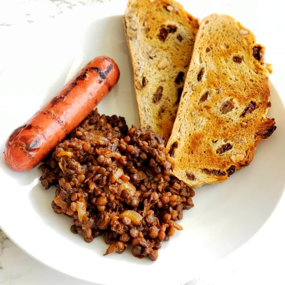 Barbecue Baked Lentils with grilled hot dog and toasted bread on a white plate