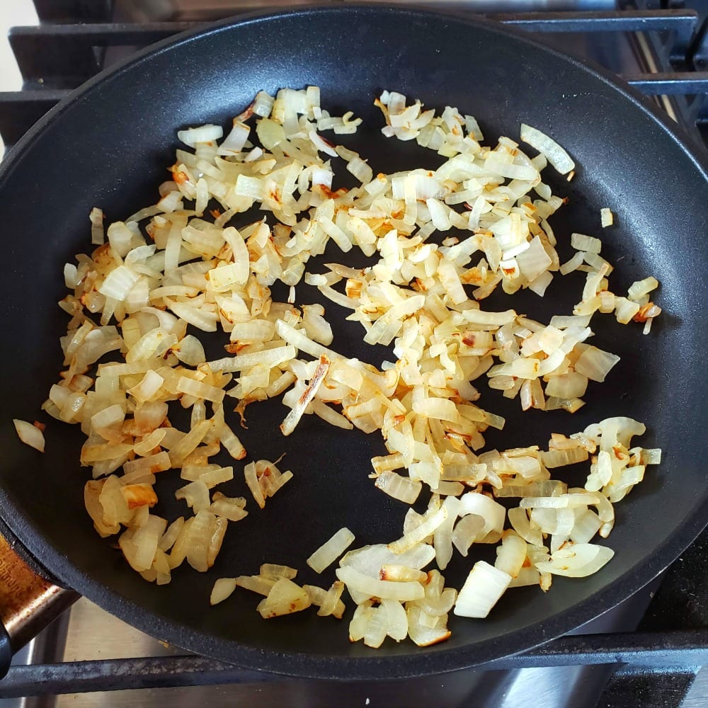 Chopped onion sauteeing in a skillet on ShockinglyDelicious.com