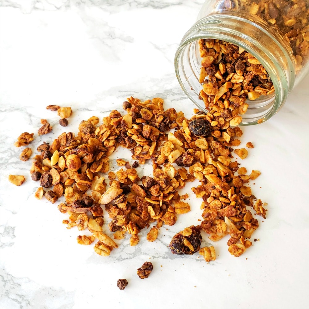 Honey Nut Granola spilling out of a jar on a white countertop