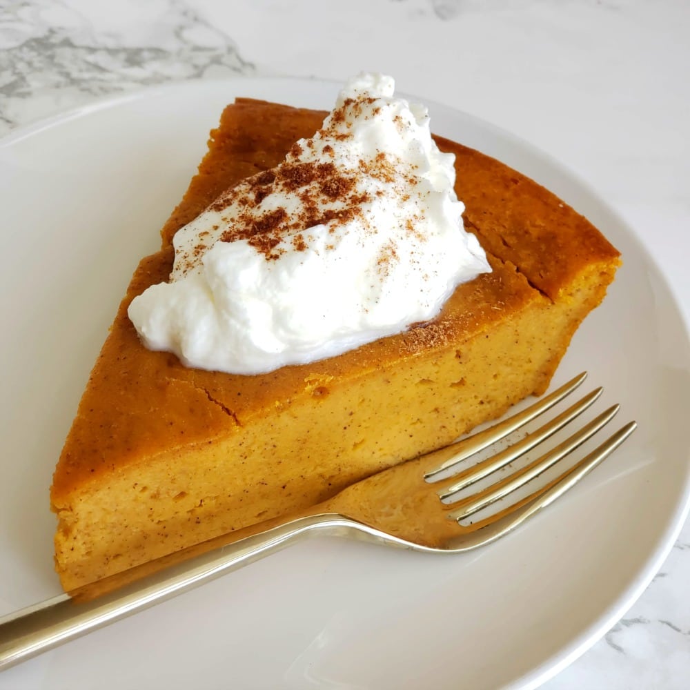 Wedge of Pumpkin Impossible Pie with dollop of whipped cream on top and a fork alongside it on a white plate on ShockinglyDelicious.com