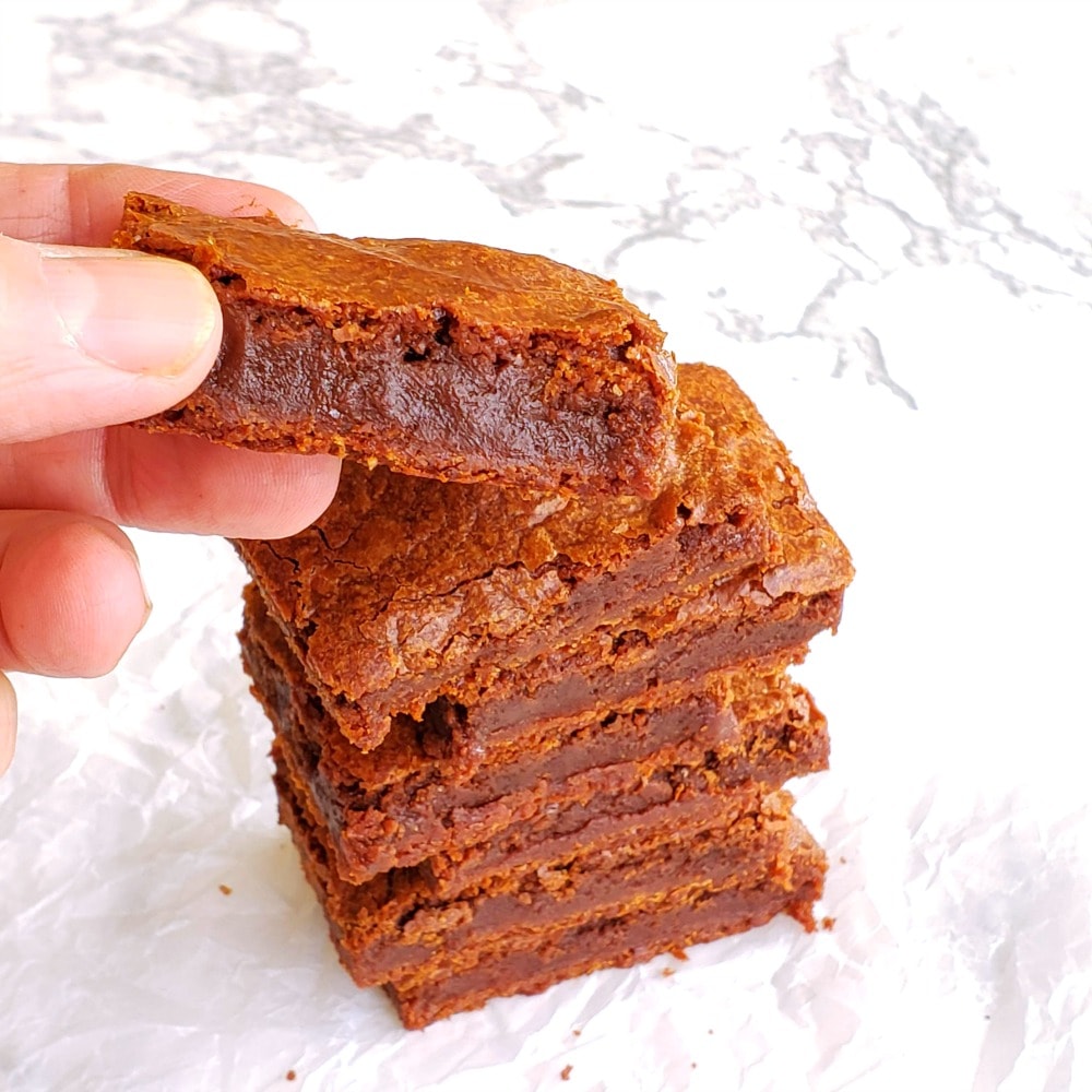 Dark Fudgy Chocolate Brownies in a stack on a white marble counter, with a hand taking the top one