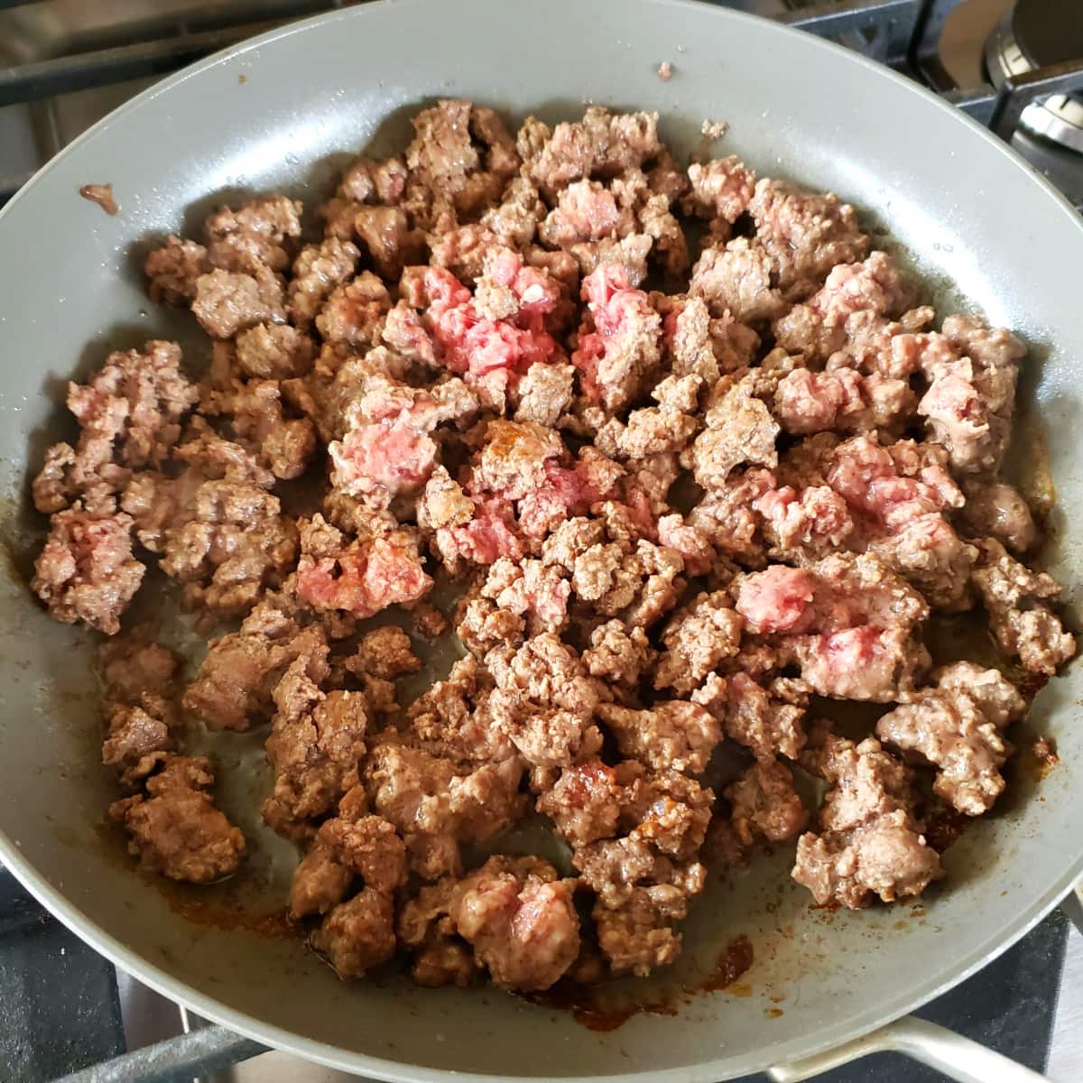 Ground beef cooking in a gray skillet