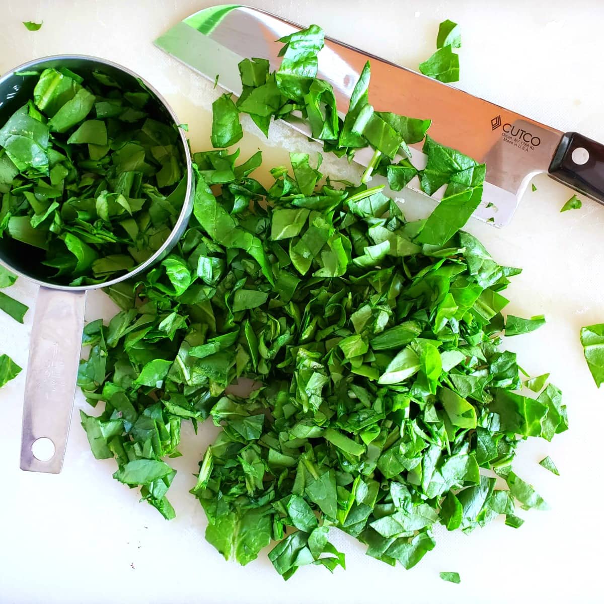 Chopping spinach on a white cutting board with a Cutco chef's knife
