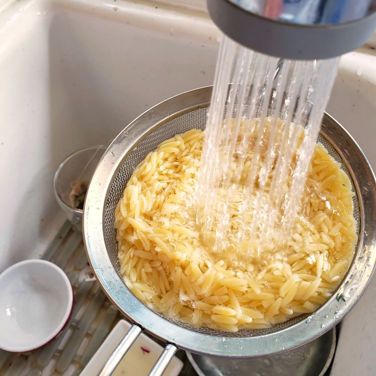 Cooked orzo being rinsed in a colander