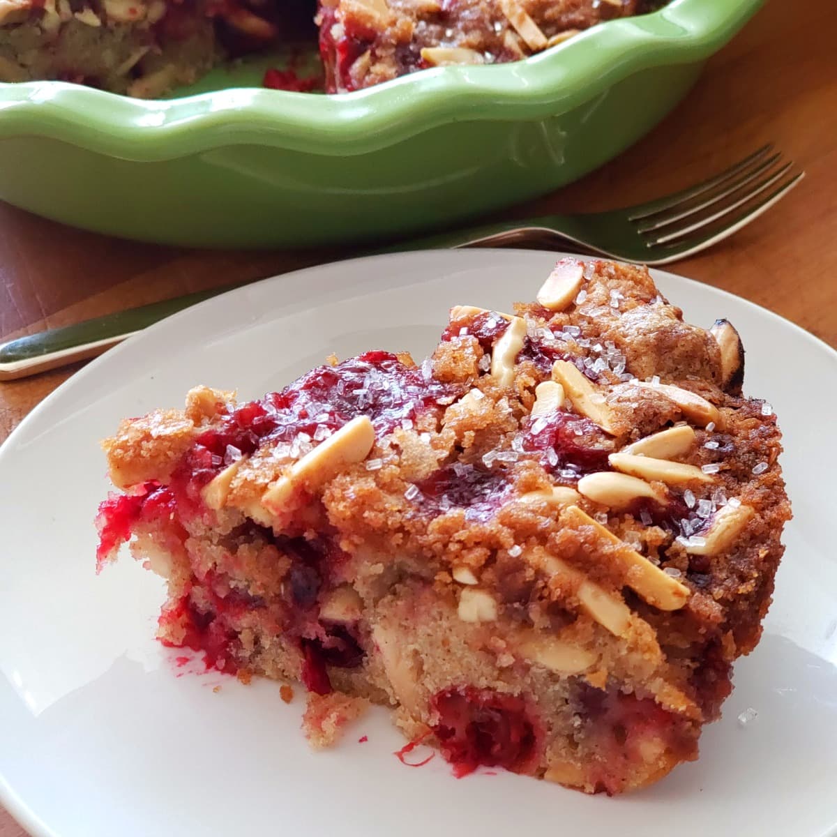 Wedge of Cranberry Breakfast Cake on a white plate with green pie dish in background on ShockinglyDelicious.com