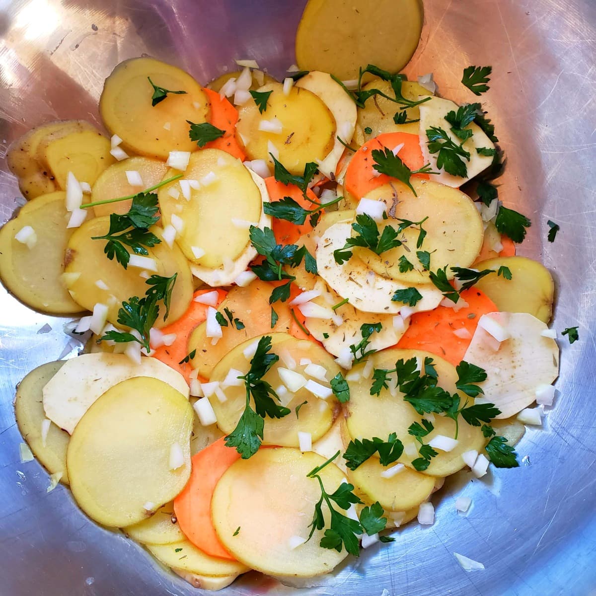 Potatoes layeres in a big mixing bowl with fresh parsley and onions