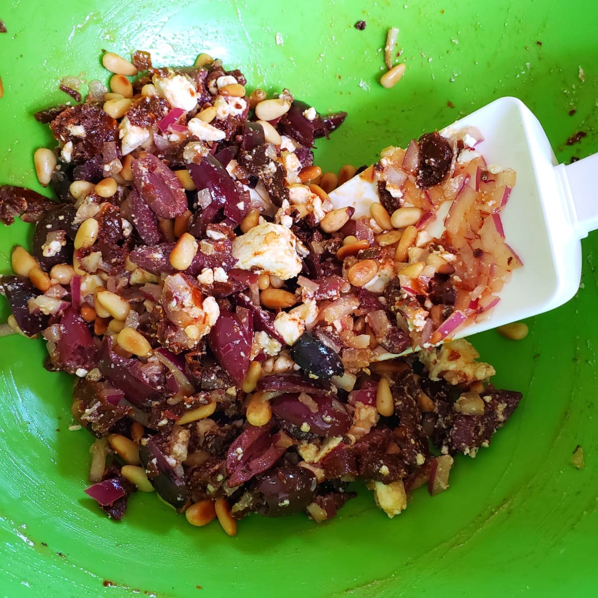 Olive mixture in a green mixing bowl with a white spatula