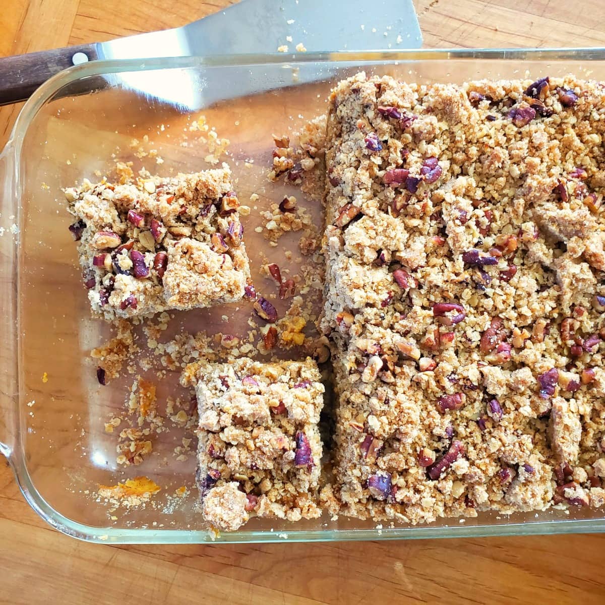 Cutting bars with a spatula and bars are in a glass baking dish on a wooden board