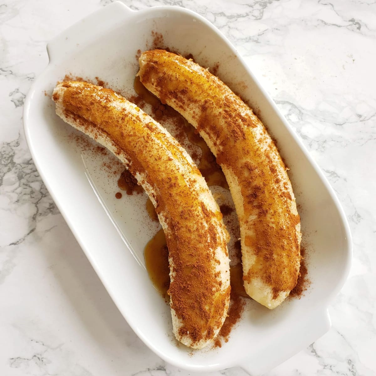 2 Bananas in a white baking dish with maple and cinnamon on top